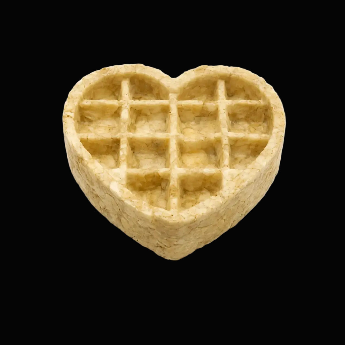 A heart-shaped waffle-shaped treat or snack piece with a grid pattern, isolated on a  black background.