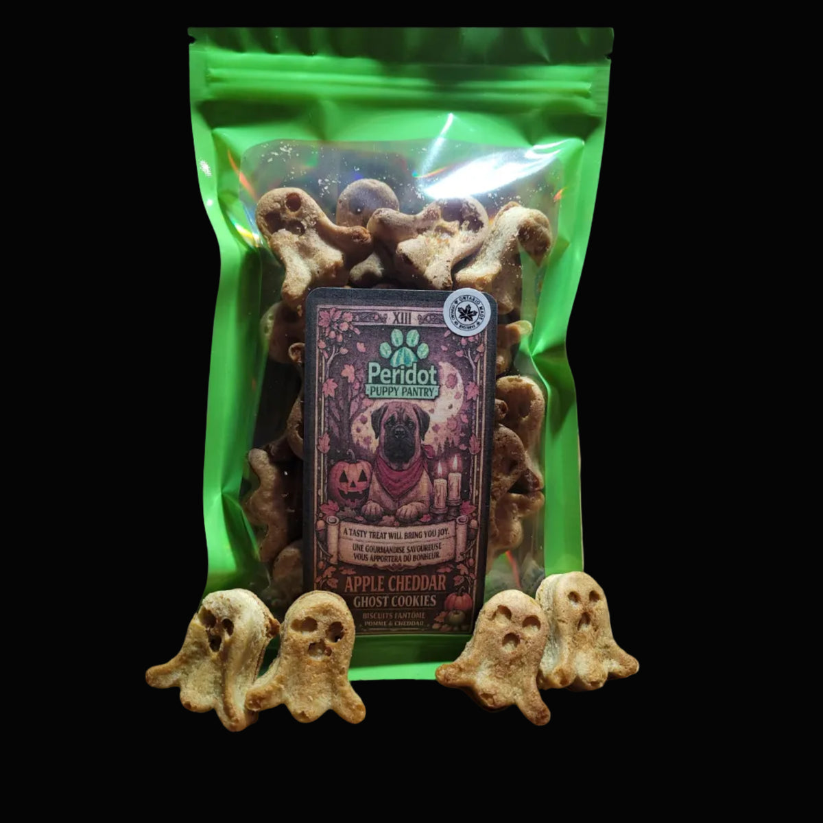 A green bag of Peridot Puppy Fancy Apple Cheddar Ghost Cookies dog treats  with several small ghost-shaped cookies placed in front of the package.